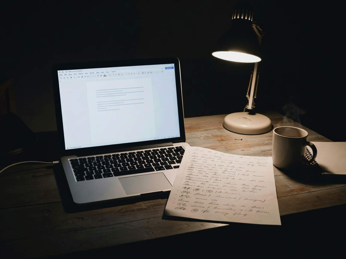 Laptop and handwritten document outline on a dimly lit practical workspace